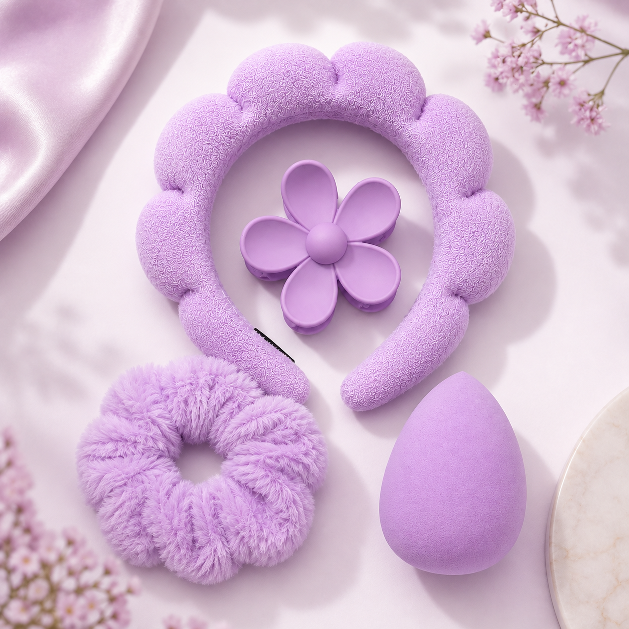 Accesorios de belleza lila del set: diadema, scrunchie, esponja de maquillaje y pinza en forma de flor.